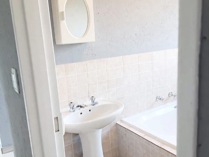 A functional bathroom featuring a pedestal basin, built-in bathtub, and tiled splashback, offering a clean, neutral space ready for potential cosmetic updates.