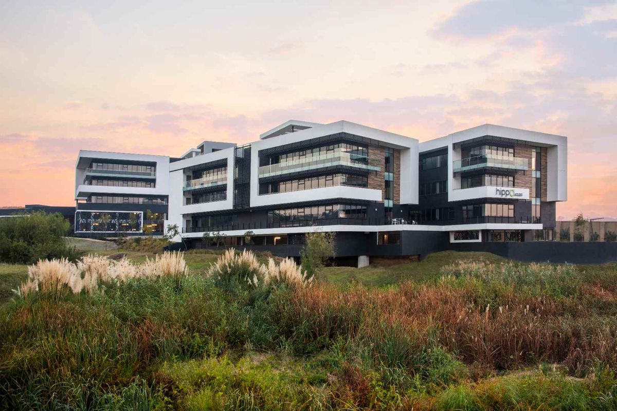 A modern multi-story apartment complex featuring contemporary architectural design, glass balconies, and clean geometric lines, set against a natural landscape.