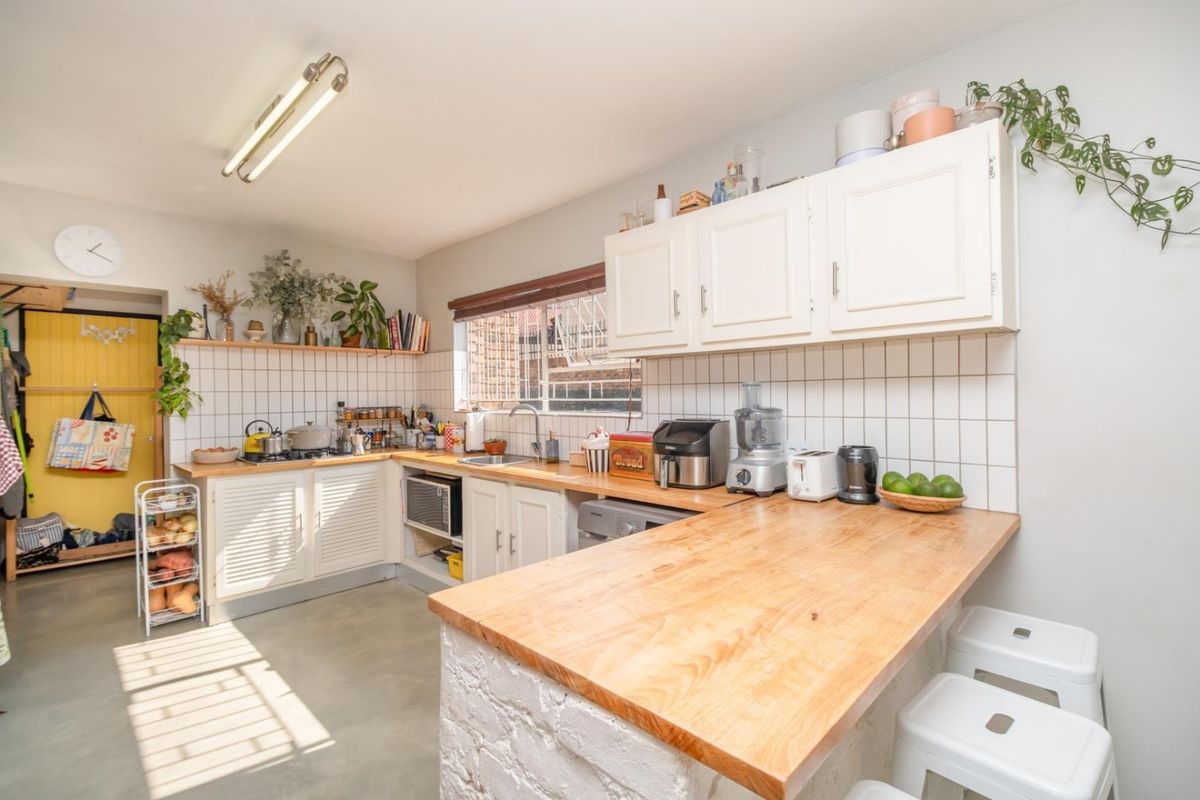 A functional kitchen featuring wooden countertops, white cabinetry, a tiled backsplash, and a breakfast bar with a brick base.