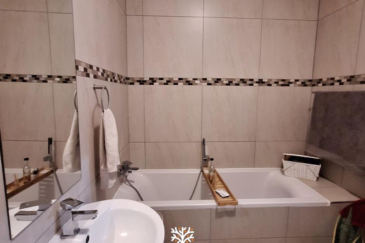 A modern bathroom featuring a built-in bathtub, wall-mounted basin with chrome mixer tap, and neutral floor-to-ceiling wall tiling.