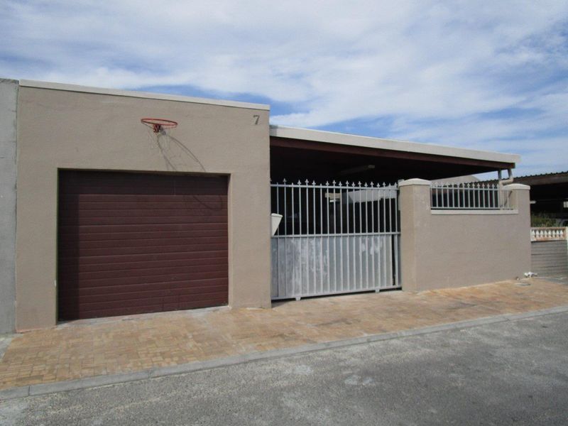 Front exterior view of the property featuring a single garage, covered carport, and secure gated entrance with paved driveway.