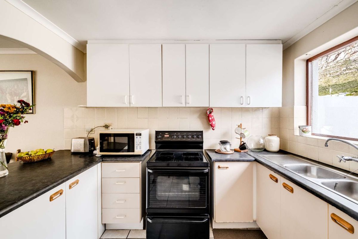 A functional kitchen featuring white cabinetry, dark laminate countertops, a stainless steel double sink, and a freestanding electric stove with a tiled backsplash.