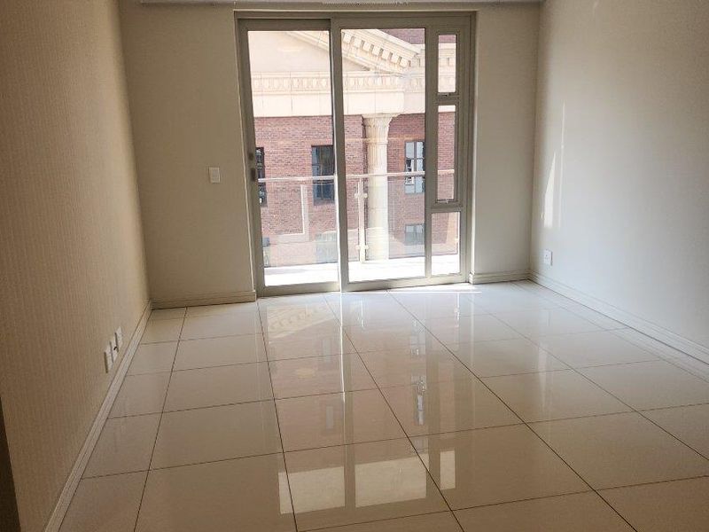 A bright, empty living room featuring polished tiled flooring, recessed ceiling lights, and a large sliding glass door leading to an outdoor balcony.