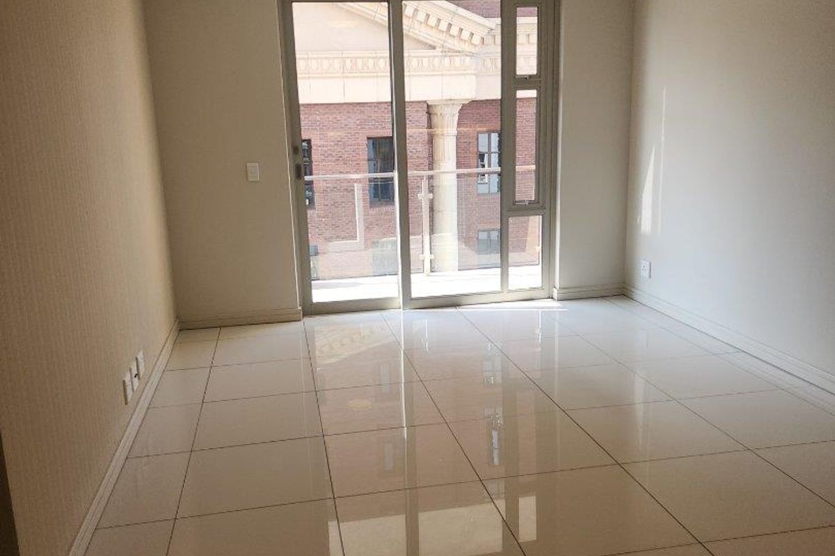 A bright, empty living room featuring polished tiled flooring, recessed ceiling lights, and a large sliding glass door leading to an outdoor balcony.