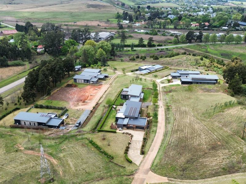 Aerial view of a residential estate featuring multiple modern dwellings with metal roofs, solar panels, and established landscaping set within a rural landscape.