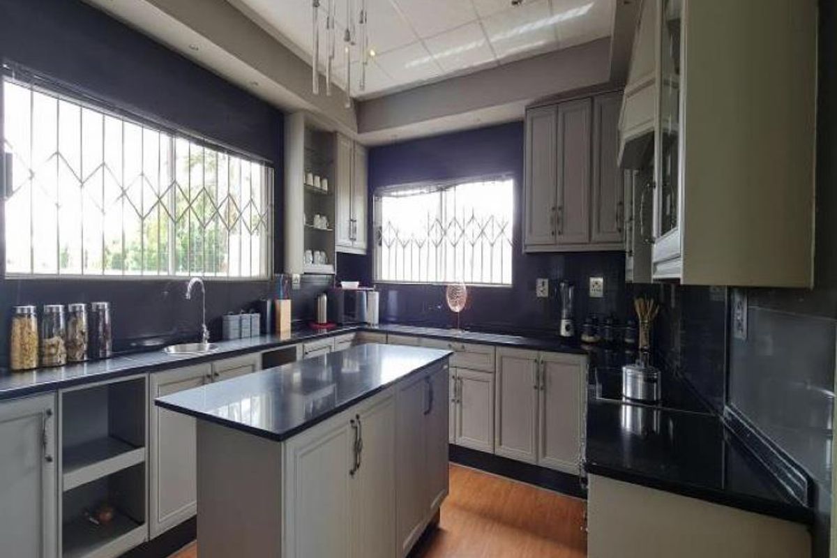 Modern kitchen featuring a central island, dark stone countertops, light-toned cabinetry, and security bars on the windows.