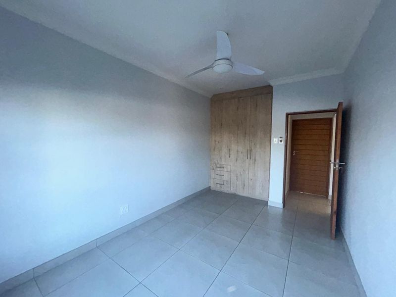 A clean, empty bedroom featuring neutral tiled flooring, built-in wooden cupboards, and a ceiling fan, offering a versatile space ready for personalization.