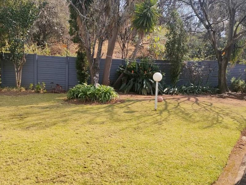A well-maintained private garden featuring a manicured lawn, mature trees, perimeter fencing, and a paved walkway.