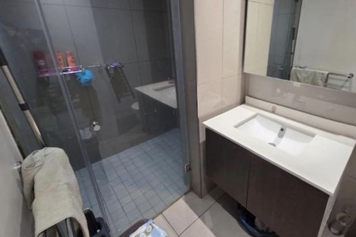 Modern bathroom featuring a vanity with integrated basin, wall-mounted mirror, and a glass-enclosed shower with tiled finishes.