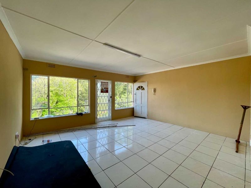 An empty living room featuring tiled flooring, security gates, and large windows providing natural light and garden views.