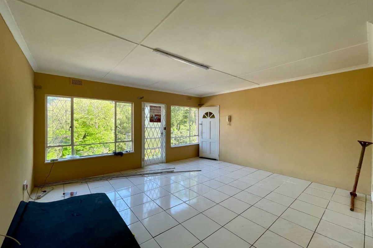 An empty living room featuring tiled flooring, security gates, and large windows providing natural light and garden views.