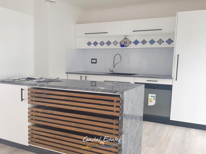 Modern kitchen featuring white cabinetry, stone countertops, a central island with timber slat detailing, and integrated appliances.