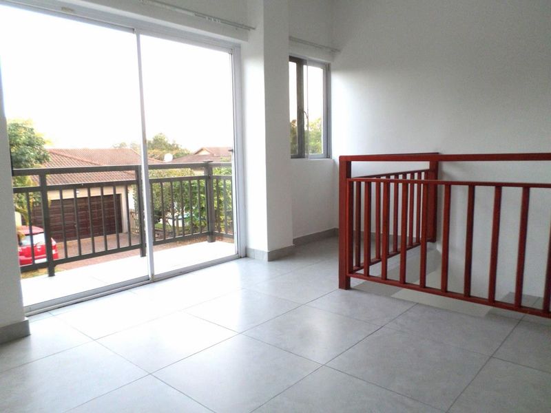 An empty upper-level landing area featuring tiled flooring, a staircase railing, and a sliding glass door leading to an outdoor balcony.