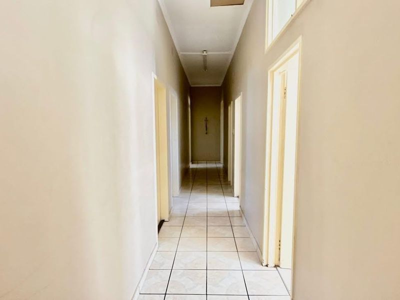 A long, neutral-toned hallway featuring tiled flooring and multiple access points to adjacent rooms.