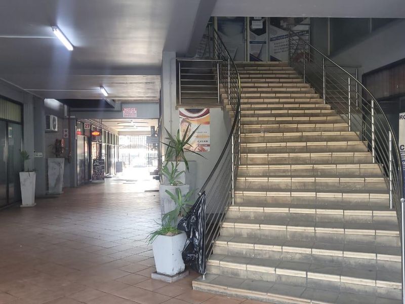 A commercial building entrance featuring a tiled walkway and a central staircase with stainless steel railings leading to upper levels.