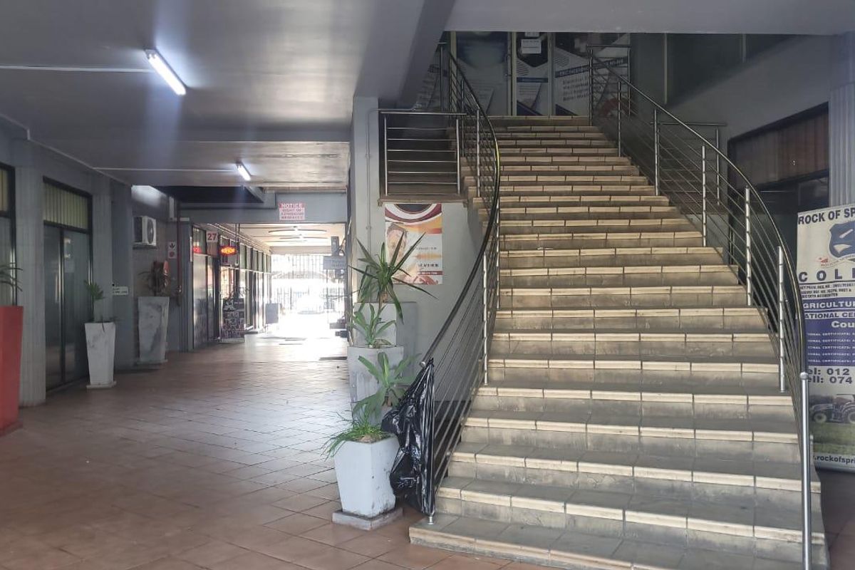 A commercial building entrance featuring a tiled walkway and a central staircase with stainless steel railings leading to upper levels.