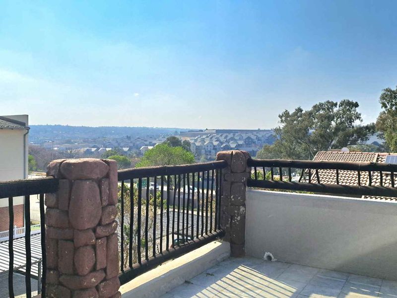 An elevated balcony featuring stone-clad pillars, metal railings, and tiled flooring, offering expansive views of the surrounding neighborhood.