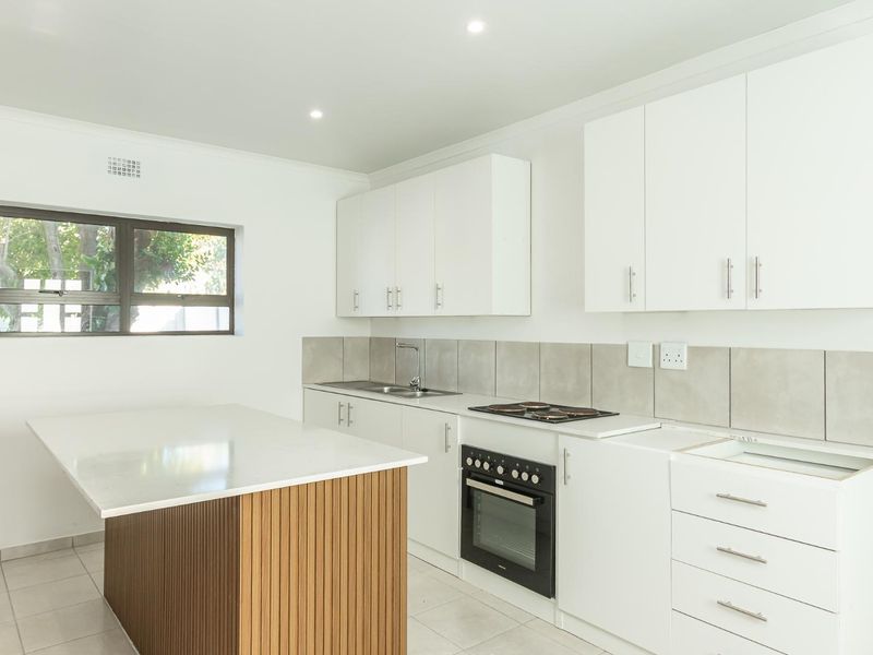 Modern kitchen featuring white cabinetry, stone countertops, a central island, built-in oven, electric hob, and neutral tiled flooring.