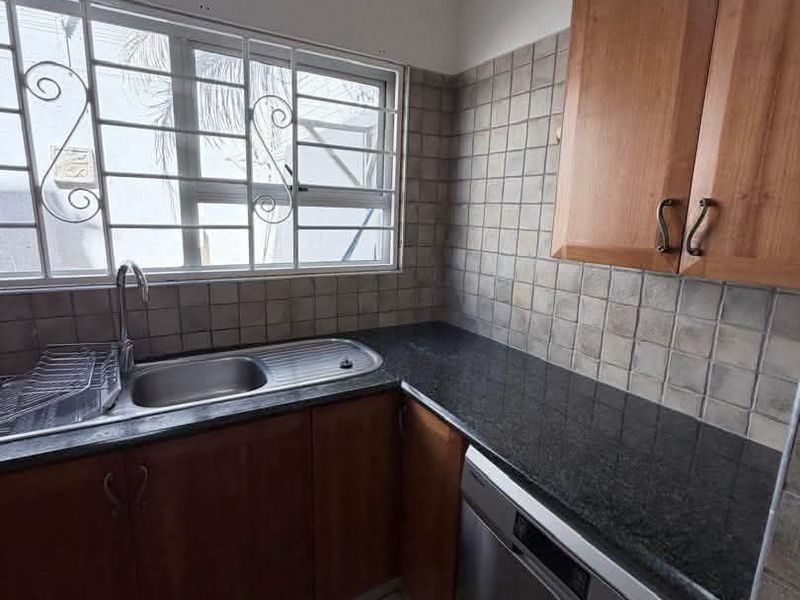A functional kitchen featuring wooden cabinetry, granite countertops, a stainless steel sink, and a tiled backsplash with security bars on the window.