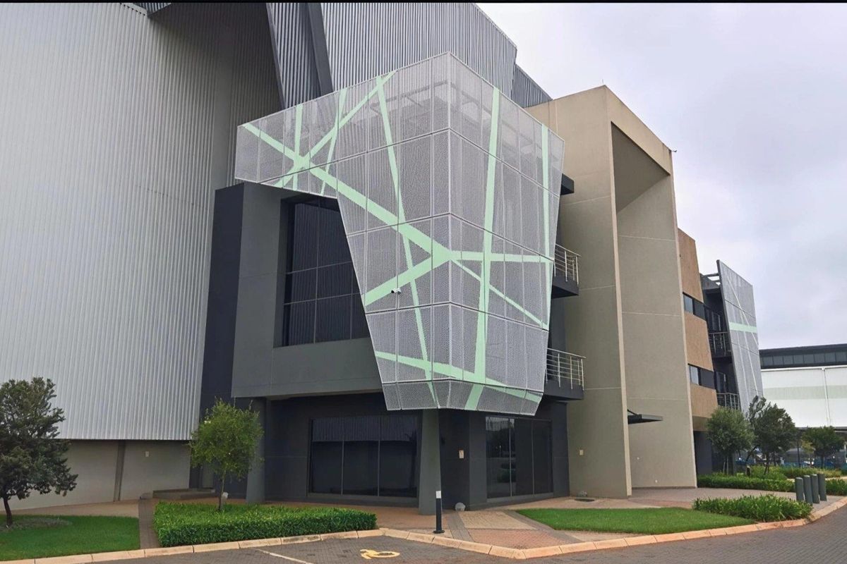 Modern industrial office building facade featuring a distinctive geometric perforated metal screen, large glass windows, and well-maintained landscaped surroundings.