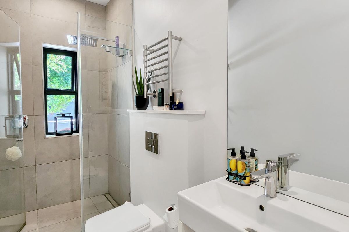 Modern bathroom featuring a walk-in glass shower, wall-mounted toilet, heated towel rail, and a sleek vanity basin with a large mirror.