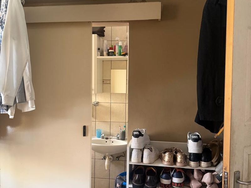 A small bathroom featuring a pedestal washbasin and tiled finishes, accessed via a sliding door with overhead built-in storage cabinetry.