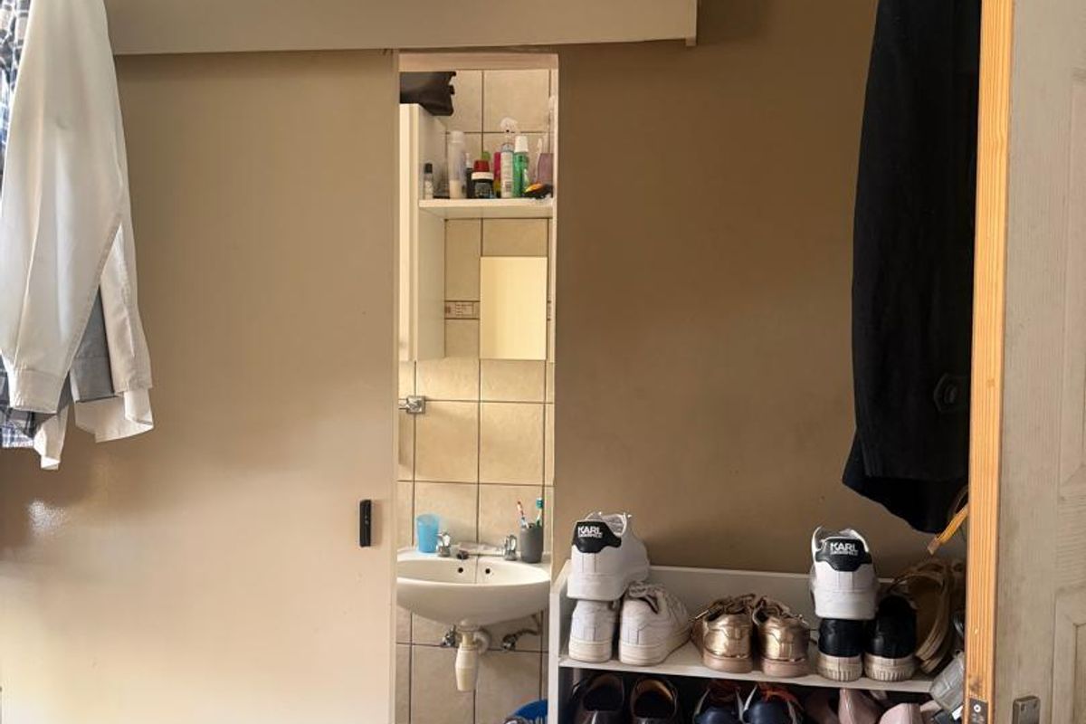 A small bathroom featuring a pedestal washbasin and tiled finishes, accessed via a sliding door with overhead built-in storage cabinetry.