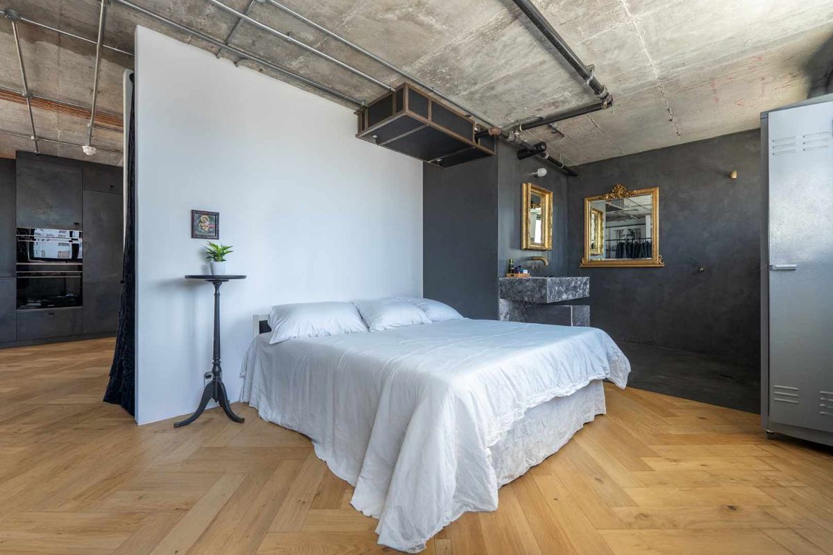 Modern industrial-style bedroom featuring exposed concrete ceilings, herringbone timber flooring, and an integrated stone vanity basin with dark cabinetry.