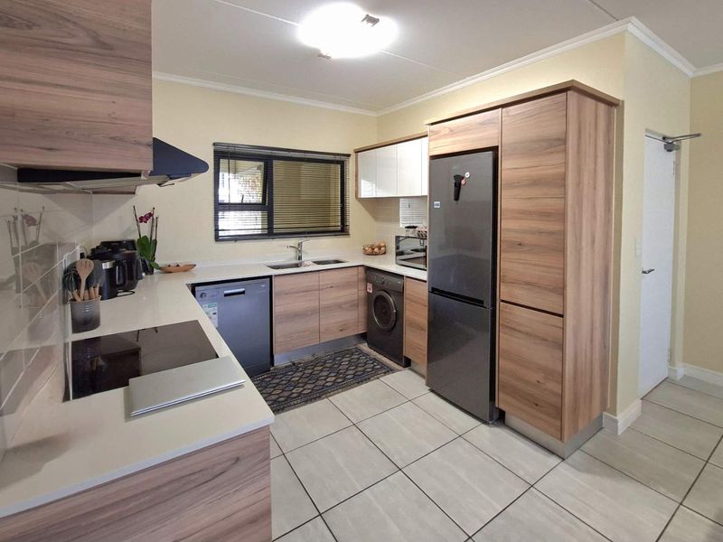 Modern kitchen featuring wood-grain cabinetry, stone countertops, integrated appliances, and tiled flooring, offering a clean and functional workspace.