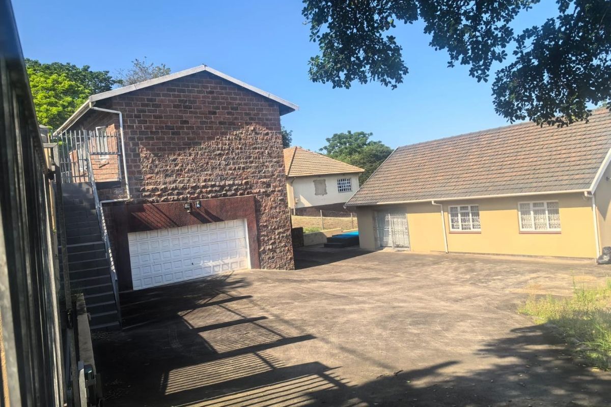 Rear exterior view showing a double garage with an external staircase, concrete driveway, and adjacent residential building structure.