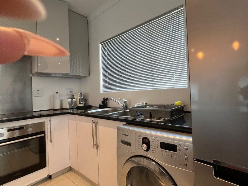 Modern kitchen featuring white cabinetry, dark countertops, stainless steel appliances, and tiled flooring with a window providing natural light.