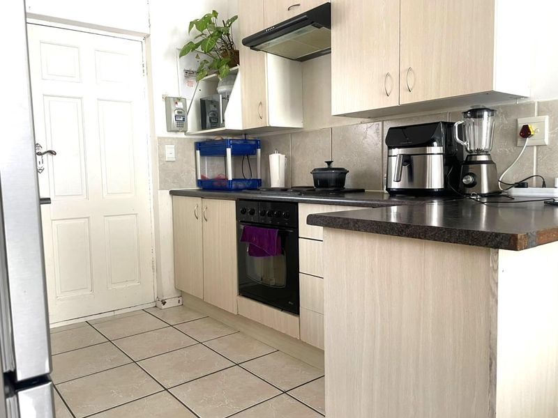 A functional kitchen featuring light wood-finish cabinetry, dark laminate countertops, built-in oven, hob, and extractor fan with tiled flooring and backsplash.