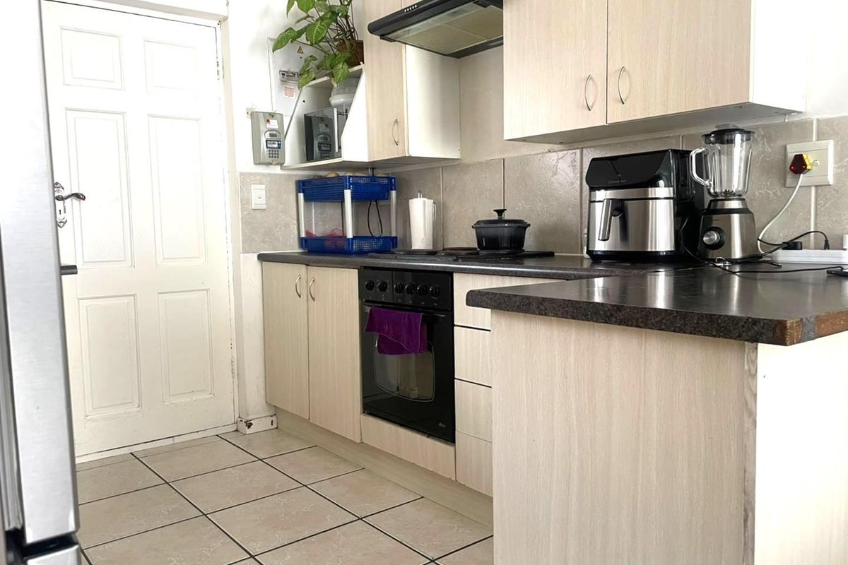 A functional kitchen featuring light wood-finish cabinetry, dark laminate countertops, built-in oven, hob, and extractor fan with tiled flooring and backsplash.