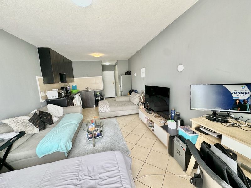 Open-plan living area featuring tiled flooring and a compact kitchen with built-in cabinetry, offering a functional layout for modern apartment living.