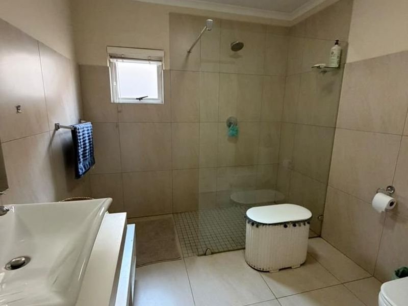 A functional bathroom featuring a walk-in shower with a glass screen, wall-mounted basin, and neutral floor-to-ceiling tiling.