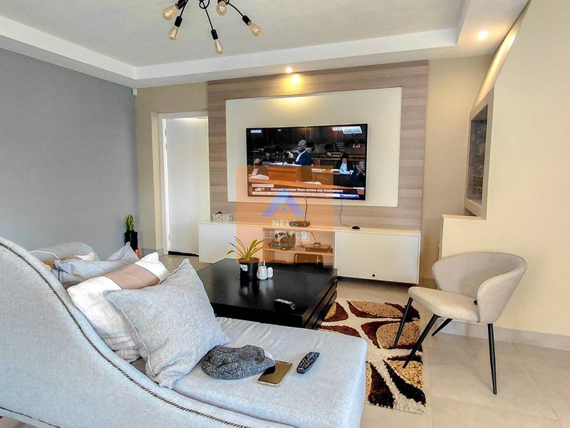 A modern living room featuring a built-in media wall, recessed ceiling lighting, and neutral tiled flooring.