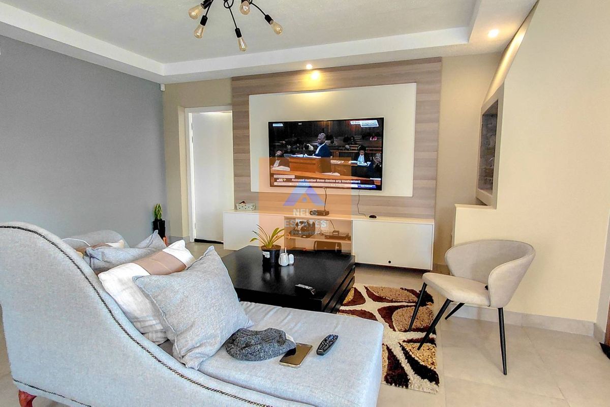 A modern living room featuring a built-in media wall, recessed ceiling lighting, and neutral tiled flooring.