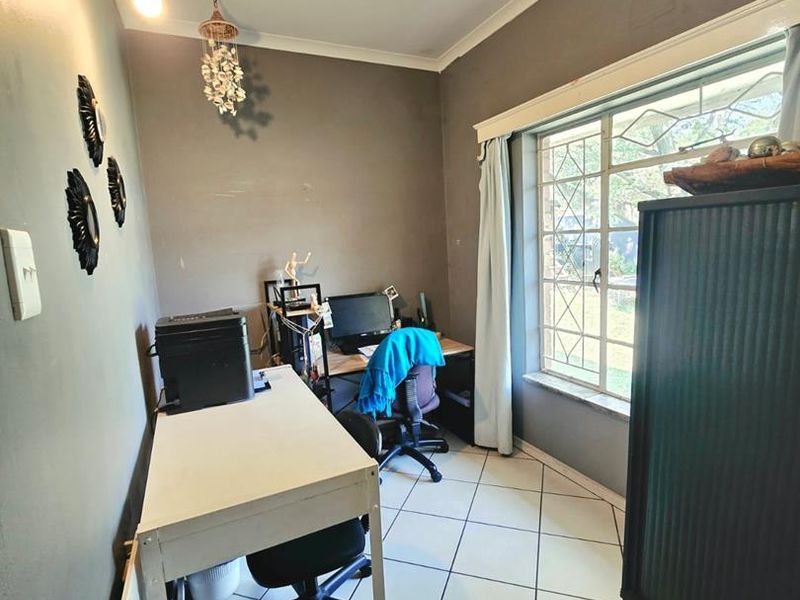 A functional home office space featuring diamond-patterned floor tiles, neutral wall tones, and a large metal-framed window providing natural light.