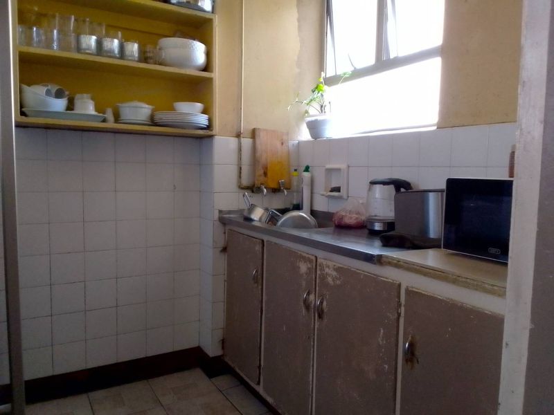 A compact kitchen featuring a stainless steel sink, tiled splashback, and dated cabinetry in need of refurbishment.