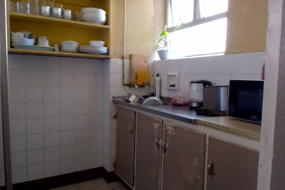 A compact kitchen featuring a stainless steel sink, tiled splashback, and dated cabinetry in need of refurbishment.