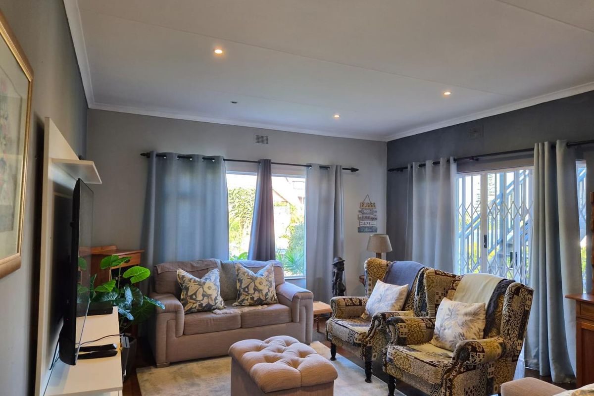 A comfortable living room featuring recessed downlights, laminate flooring, and a sliding glass door with a security gate leading to the exterior.