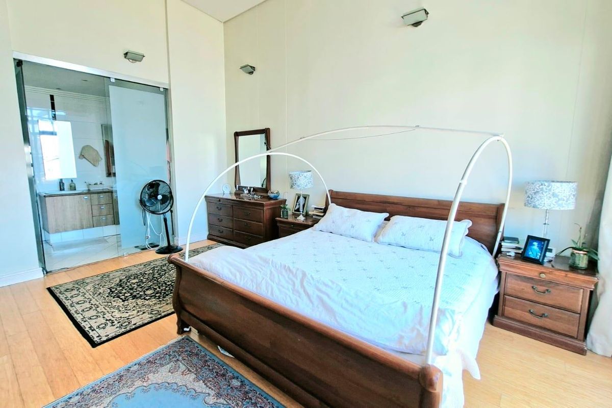 Spacious bedroom featuring light wood flooring, high ceilings, and an integrated en-suite bathroom enclosed by a modern glass partition.