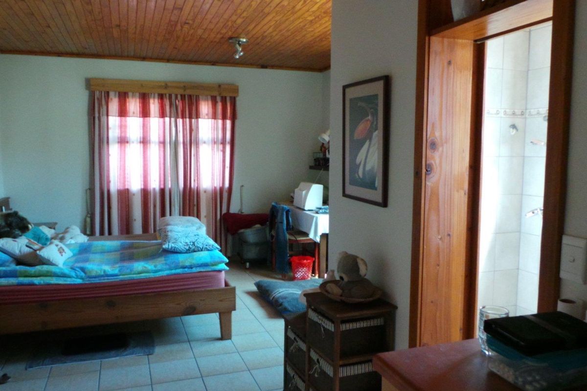 A bedroom featuring a timber-clad ceiling, tiled flooring, and an adjoining bathroom entrance, offering a functional layout with potential for modernization.