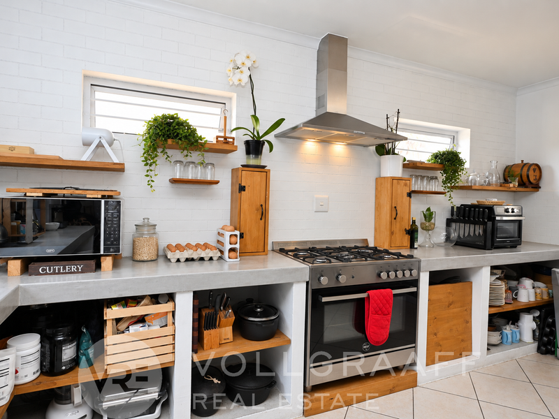 A rustic-style kitchen featuring concrete countertops, open shelving, and a built-in gas stove with a stainless steel extractor fan.