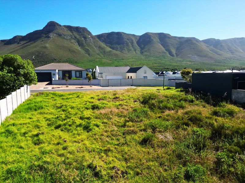 A vacant residential plot featuring natural grass cover, enclosed by boundary walls, with scenic mountain views in the background.