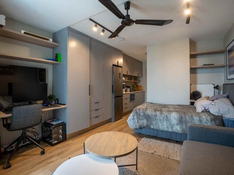 Modern open-plan studio apartment featuring integrated kitchen cabinetry, built-in storage, laminate flooring, and contemporary track lighting in a functional, well-utilized living space.