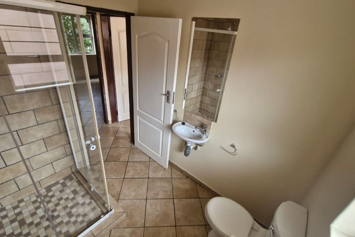 A functional bathroom featuring a glass-enclosed shower, wall-mounted basin, and toilet with tiled flooring.