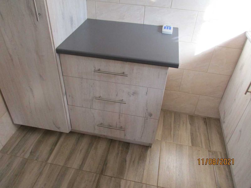 A close-up view of modern kitchen cabinetry featuring light wood-grain finish, dark grey countertop, and neutral tiled backsplash and flooring.