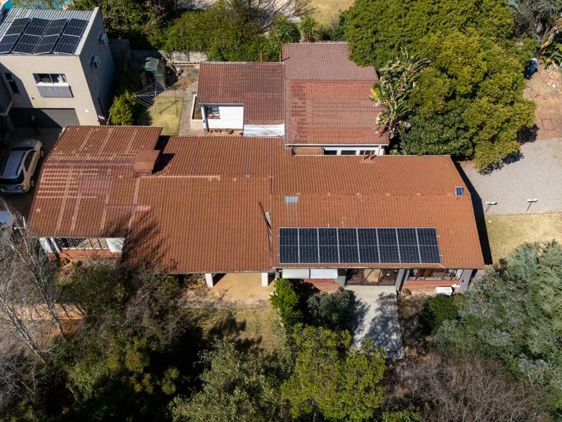 Aerial view of the property featuring a tiled roof with installed solar panels, surrounding garden, and driveway access.