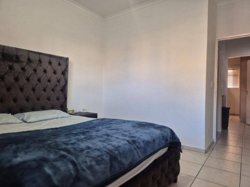 A bedroom featuring tiled flooring and coved ceilings, with a view leading into an adjacent hallway.